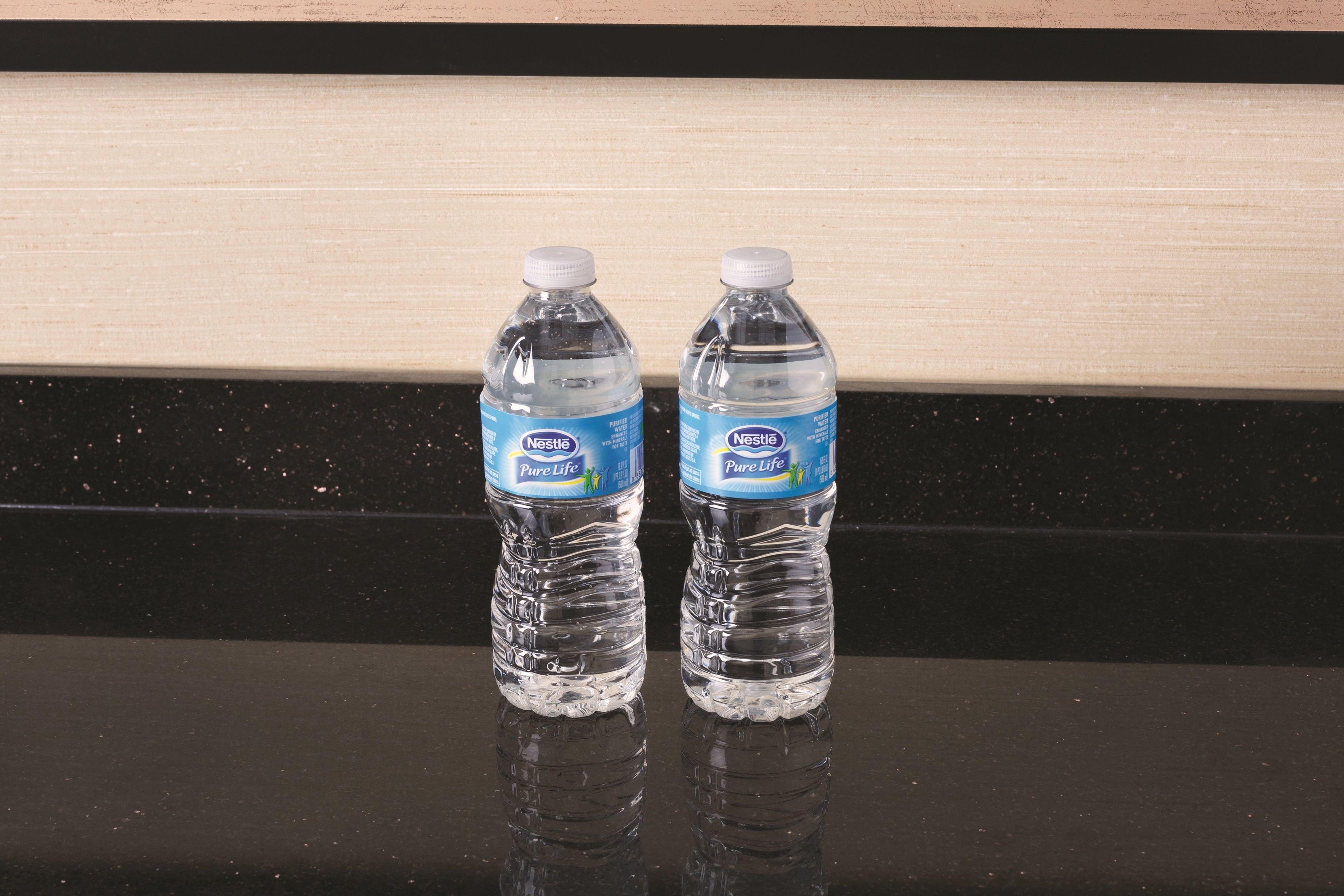 Two Nestle Pure Life water bottles on a reflective black surface against a wooden background.