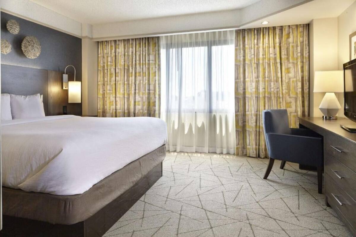 Une chambre d’hôtel avec un grand lit, un bureau avec une chaise, une télévision et une fenêtre avec des rideaux.