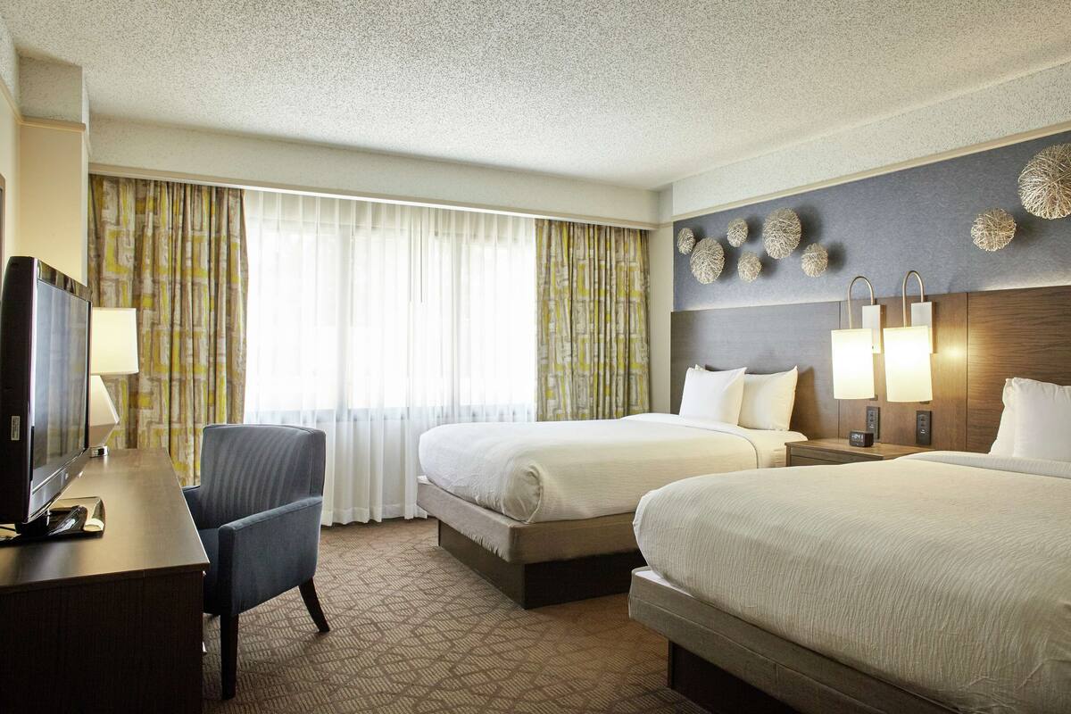 Une chambre d’hôtel avec deux lits, un bureau, une chaise et un téléviseur.