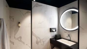 Een moderne badkamer met een marmeren wand, een ronde spiegel met verlichting, een zwarte wastafel en een handdoekhouder.