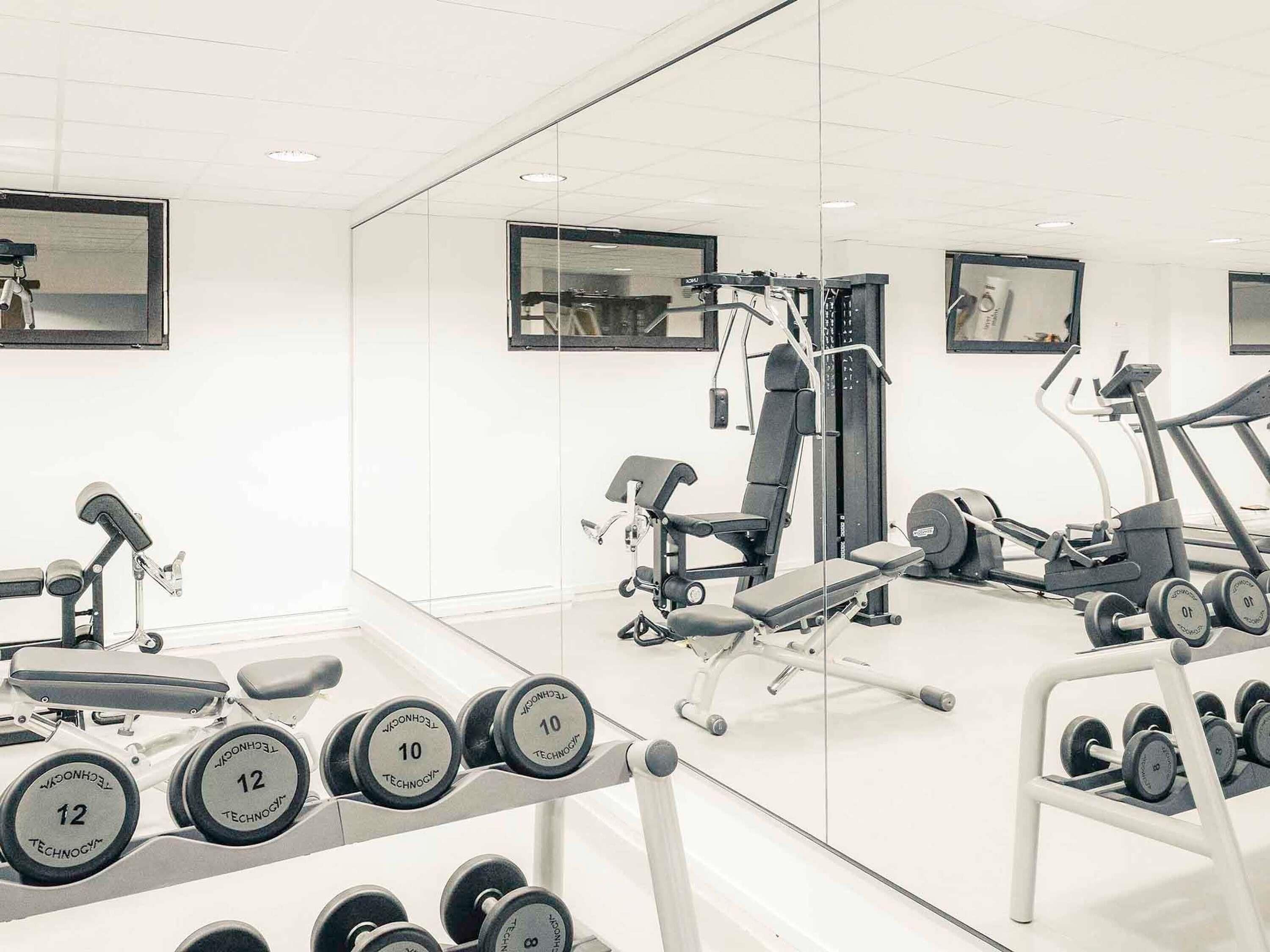 Une salle de sport équipée de matériel d’exercice, notamment des haltères, un banc et un tapis de course.