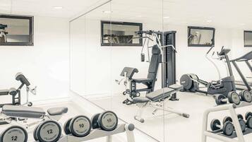 Une salle de sport équipée de matériel d’exercice, notamment des haltères, un banc et un tapis de course.