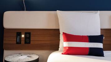 Une chambre d’hôtel avec un lit, une table de chevet et une lampe fixée au mur.