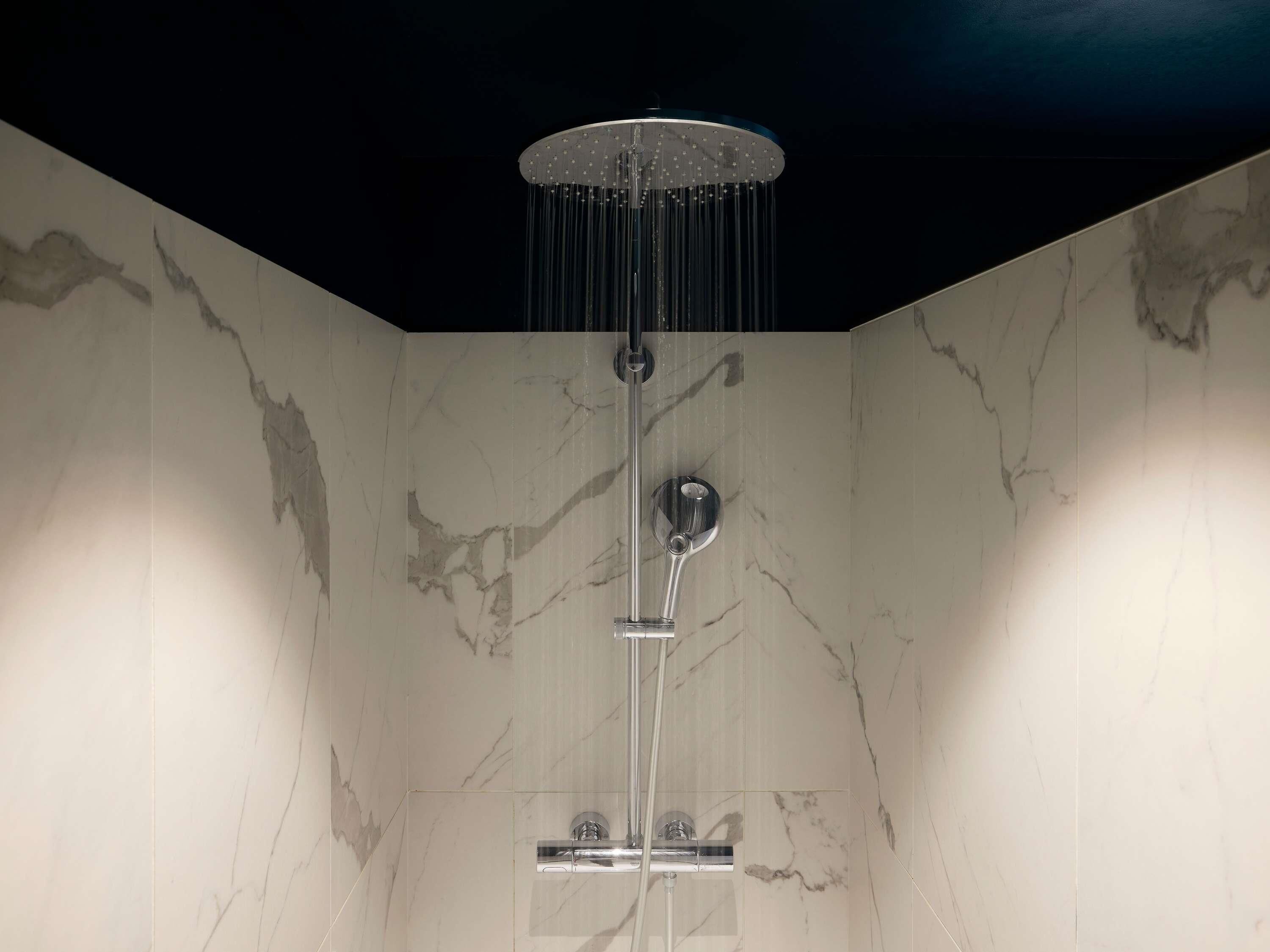 A modern shower with a rain showerhead, chrome fixtures, and marble walls.