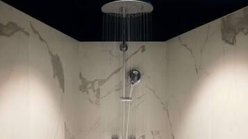 A modern shower with a rain showerhead, chrome fixtures, and marble walls.