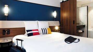 Habitació d'hotel amb un llit gran, una maleta, una petita taula de nit i un armari.