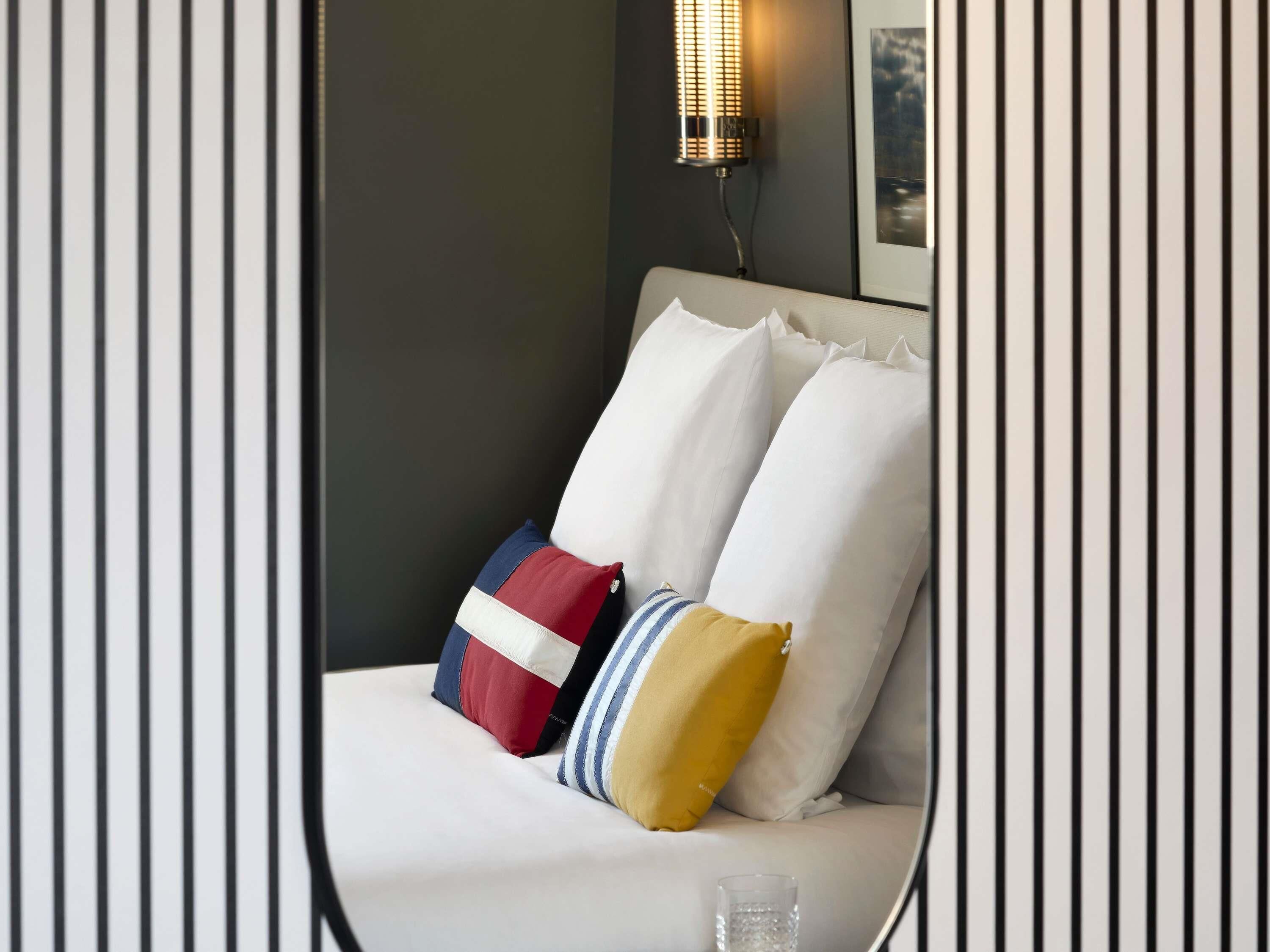 Una cama con ropa blanca, una almohada a rayas y almohadas rojas, blancas y azules.