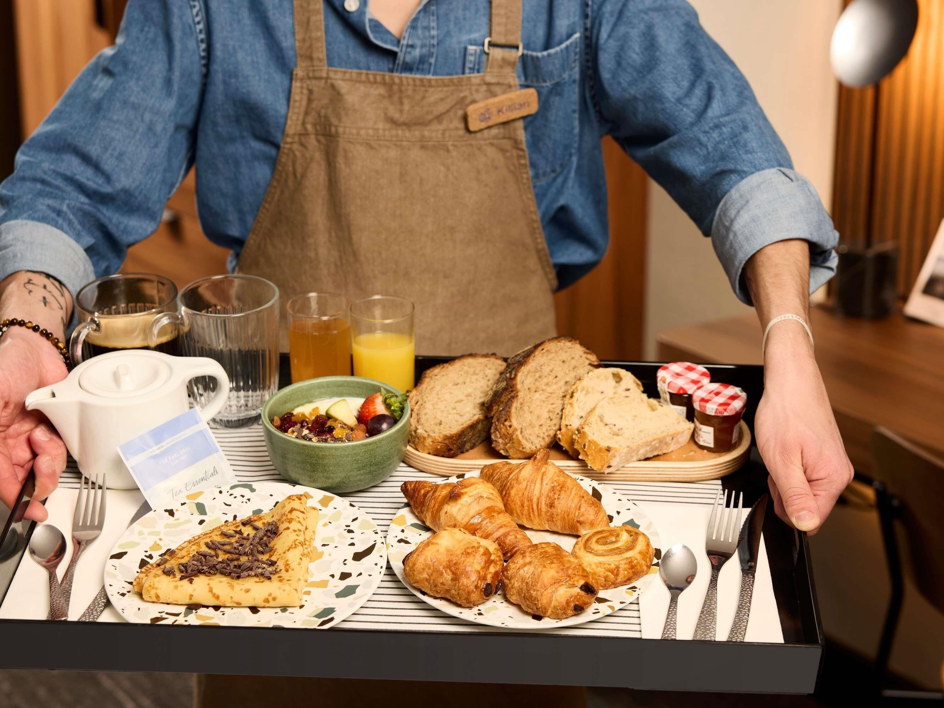 Bandeja de desayuno con croissants, pan, un bol de fruta y una tetera.