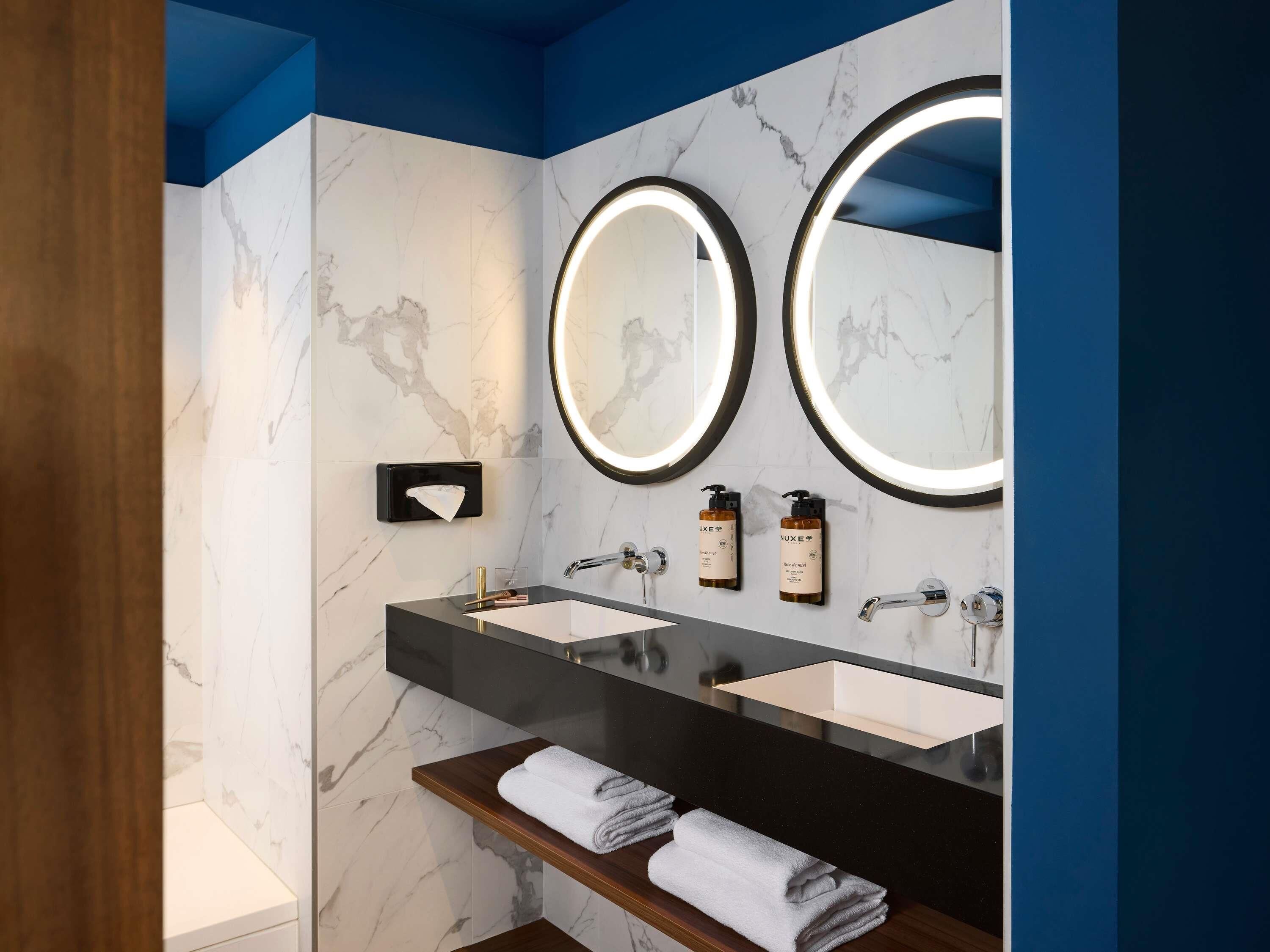 A modern bathroom with two sinks, marble walls, and a blue accent wall.