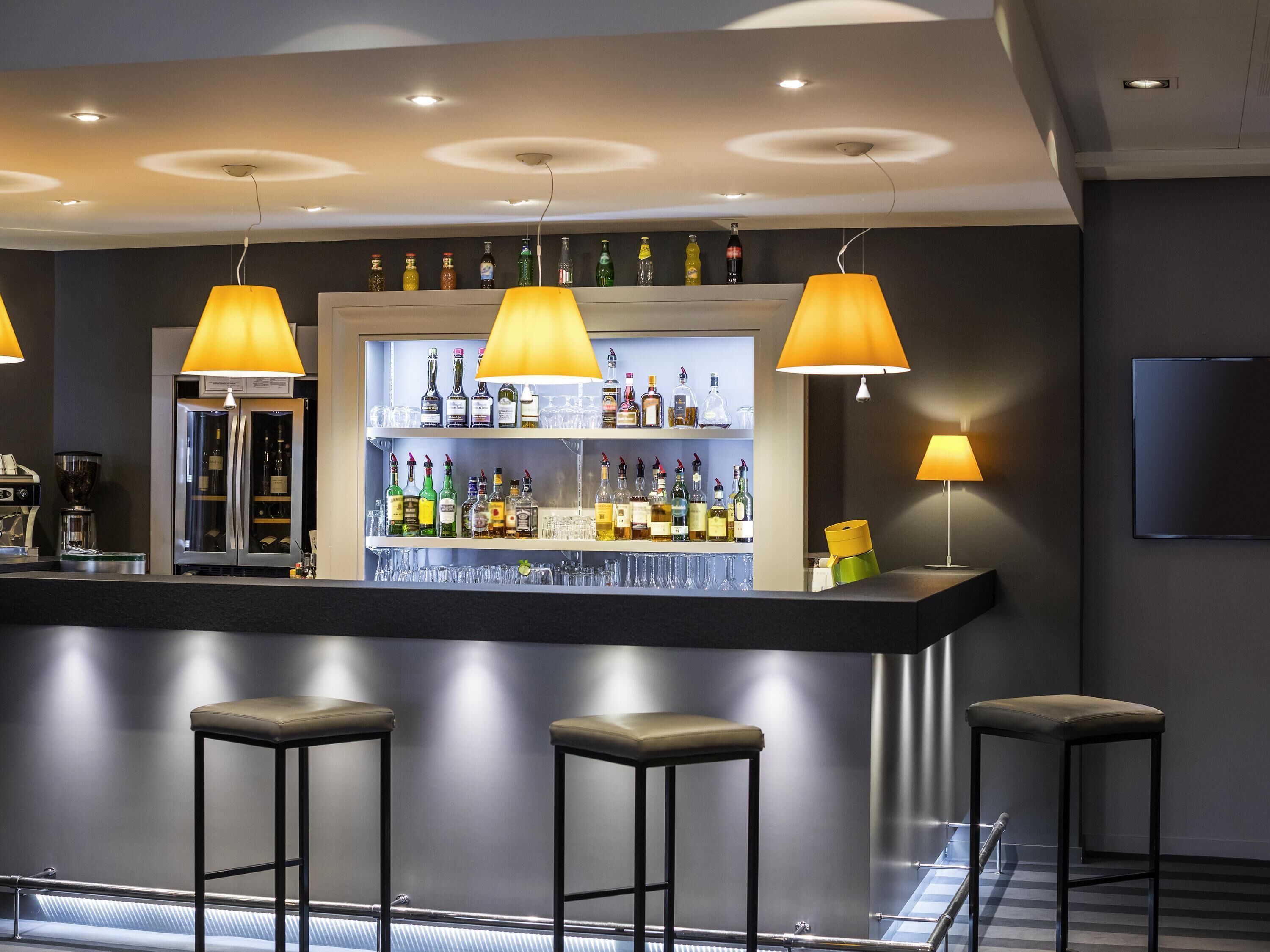 Zona de bar con mostrador, taburetes y una estantería llena de botellas.
