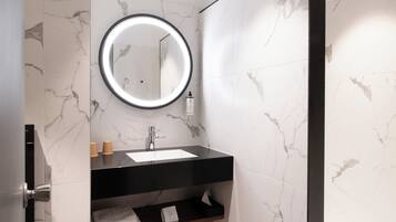A modern bathroom with a black sink, marble walls, a round mirror with a light, and a towel rack.