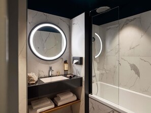 Un baño moderno con tocador de mármol, un espejo redondo con luz y ducha con cerramiento de vidrio.