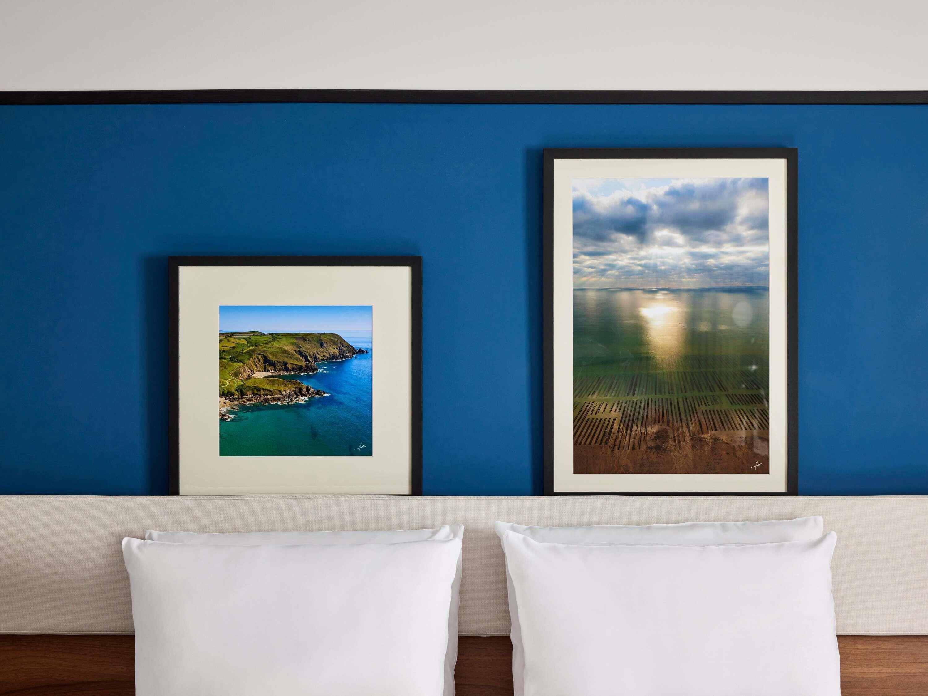 Due fotografie di paesaggi incorniciate su un muro blu, un cuscino bianco e un pavimento in legno.