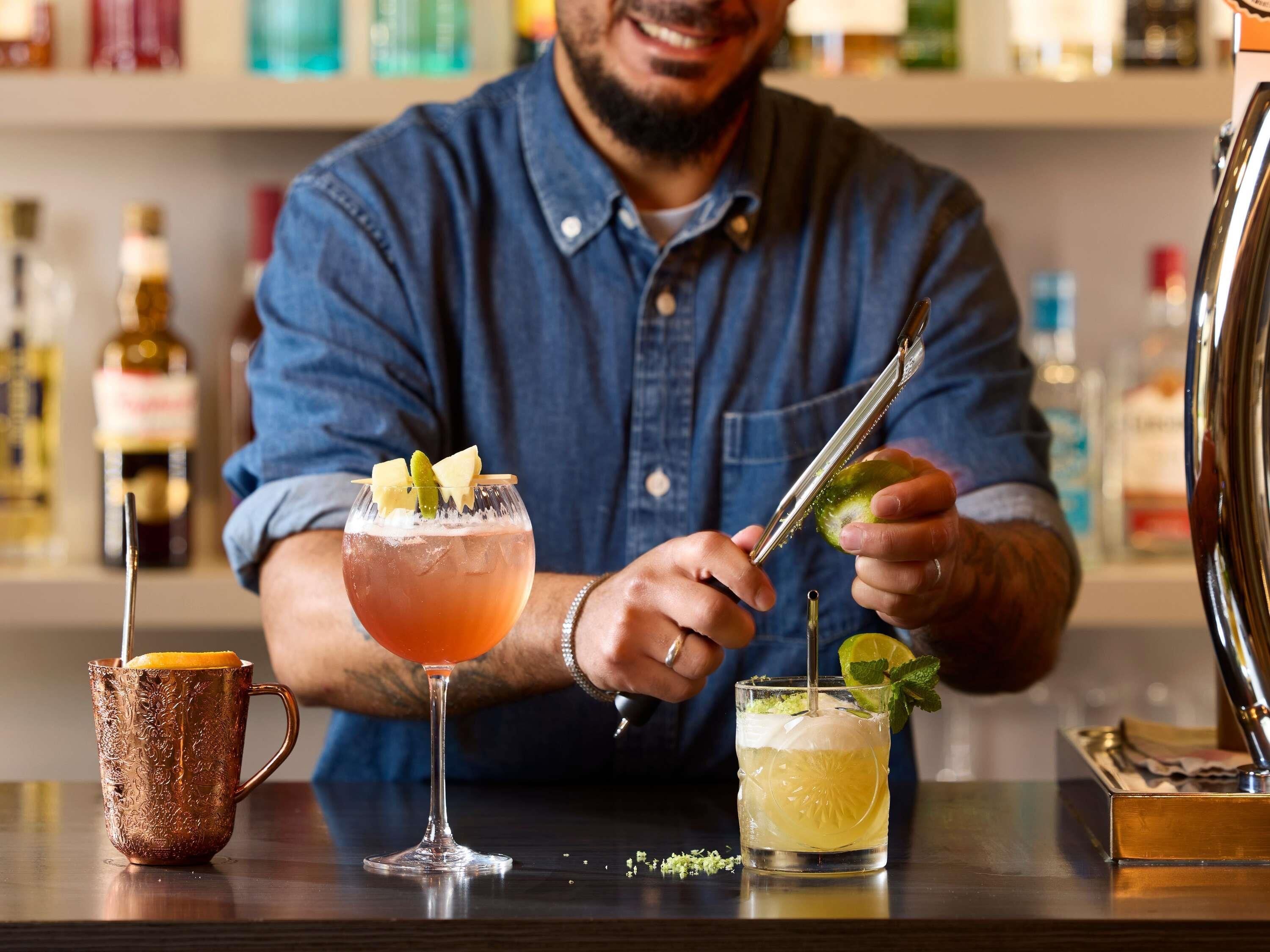 A bartender preparing drinks at a bar with a copper mug and two glasses.