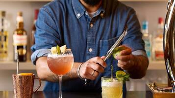 A bartender preparing drinks at a bar with a copper mug and two glasses.