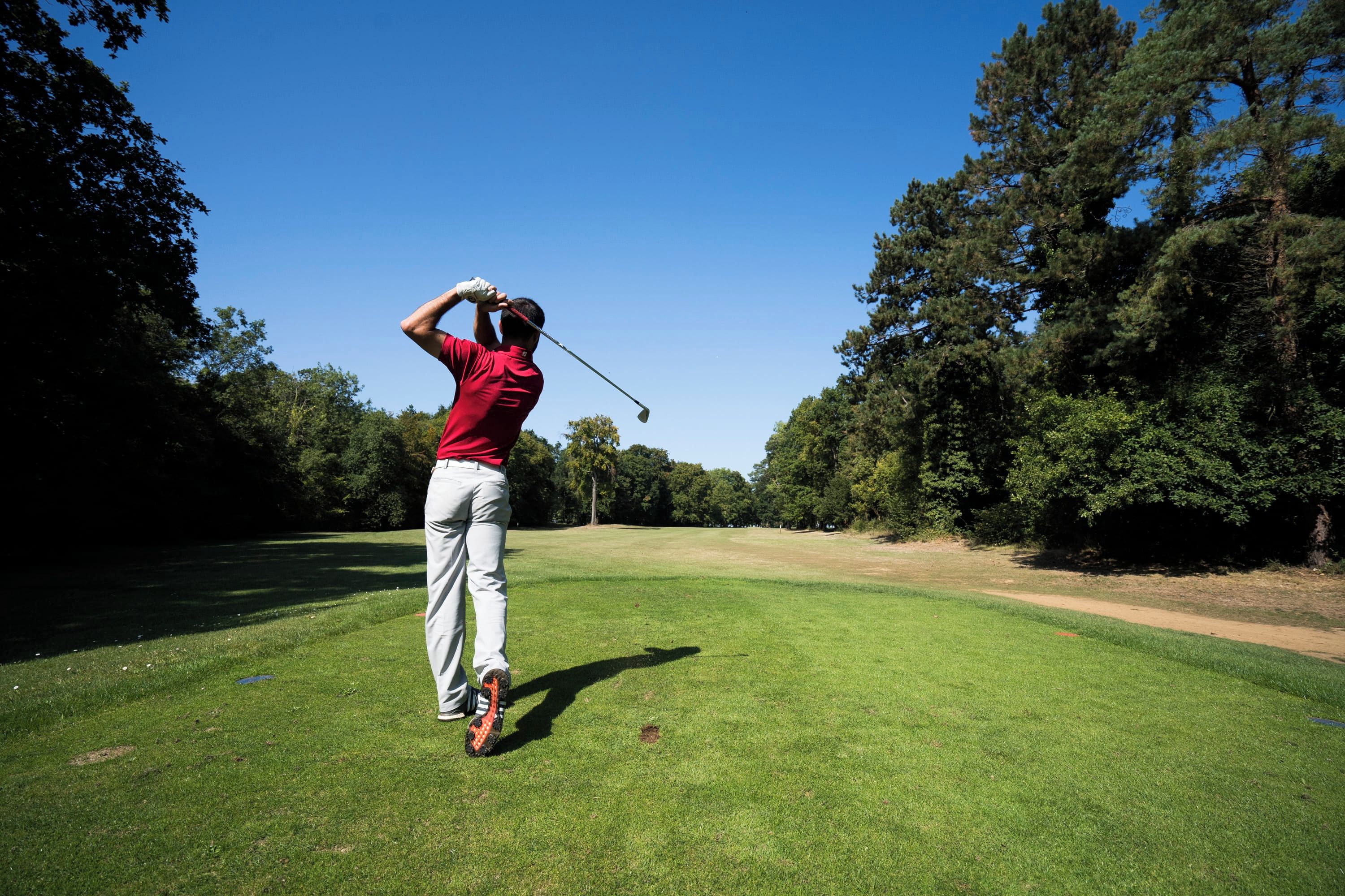 A person playing golf on a well-maintained course with trees and clear skies.