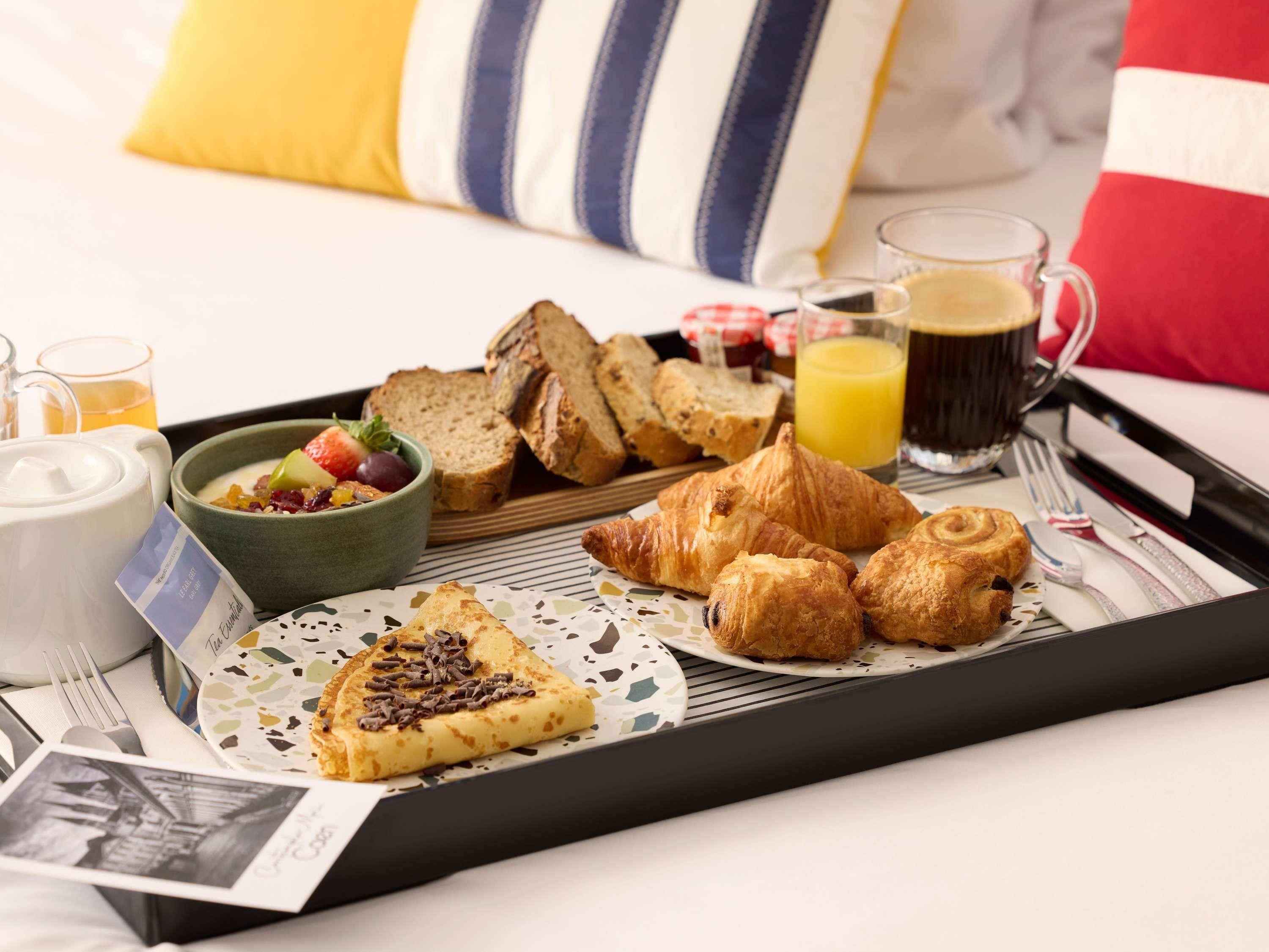 A breakfast tray with croissants, bread, a bowl of fruit, and a cup of coffee.