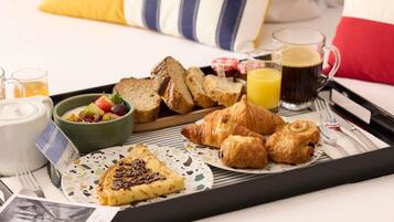 A breakfast tray with croissants, bread, a bowl of fruit, and a cup of coffee.