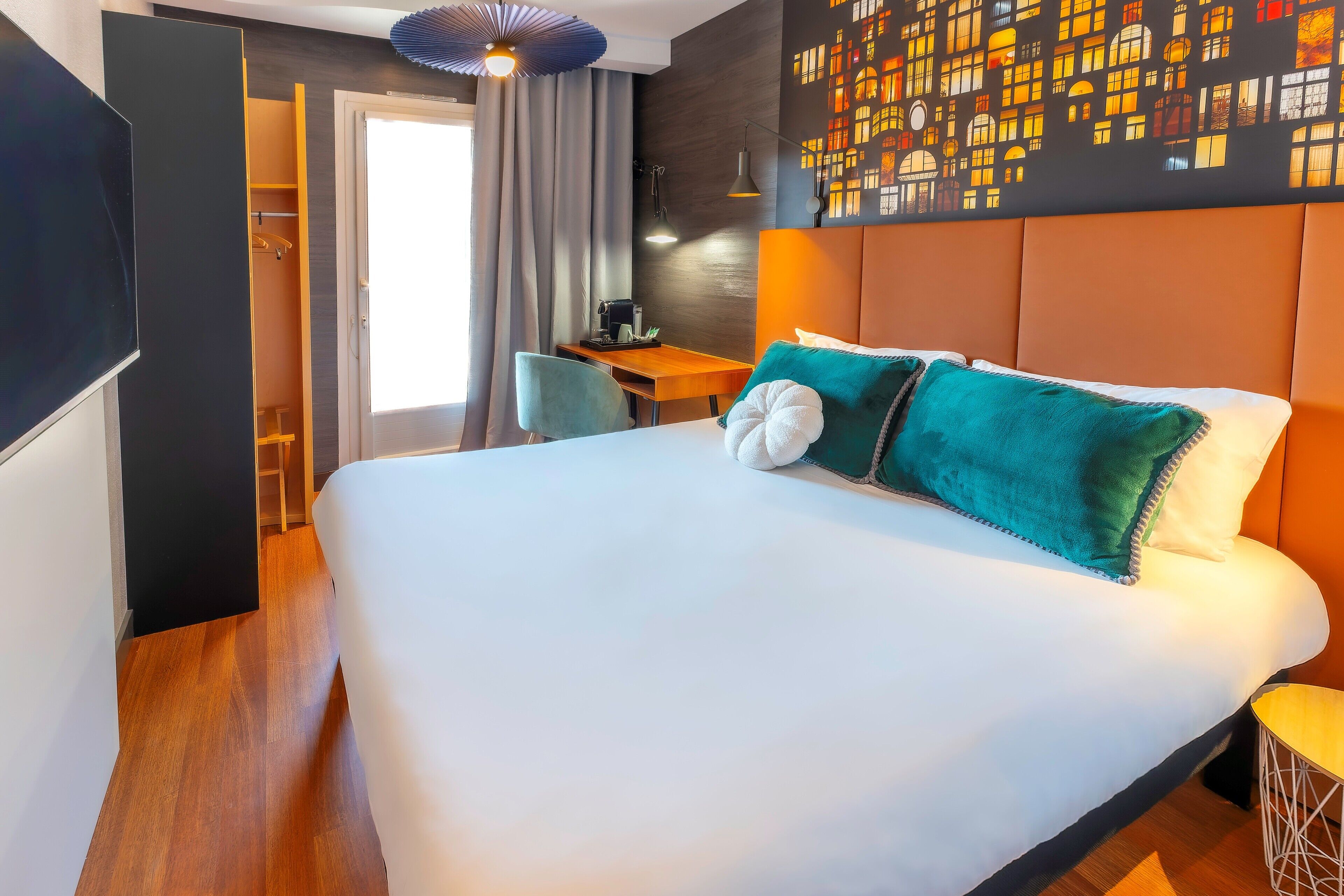 A modern hotel room with a large bed, a desk, a chair, and a television.
