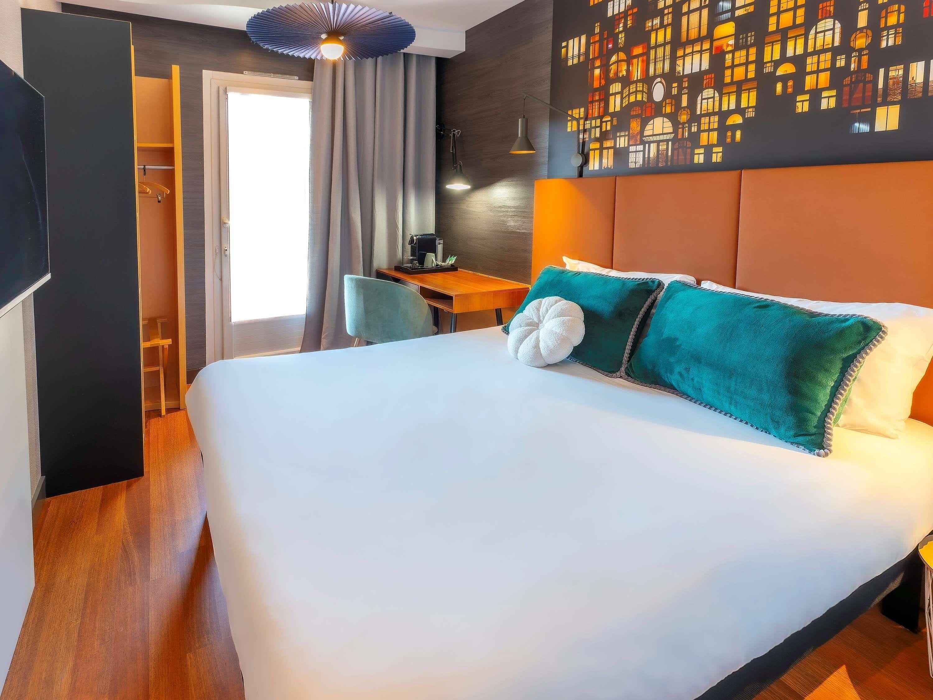 Una habitación de hotel con cama, escritorio, silla y un mural urbano en la pared.