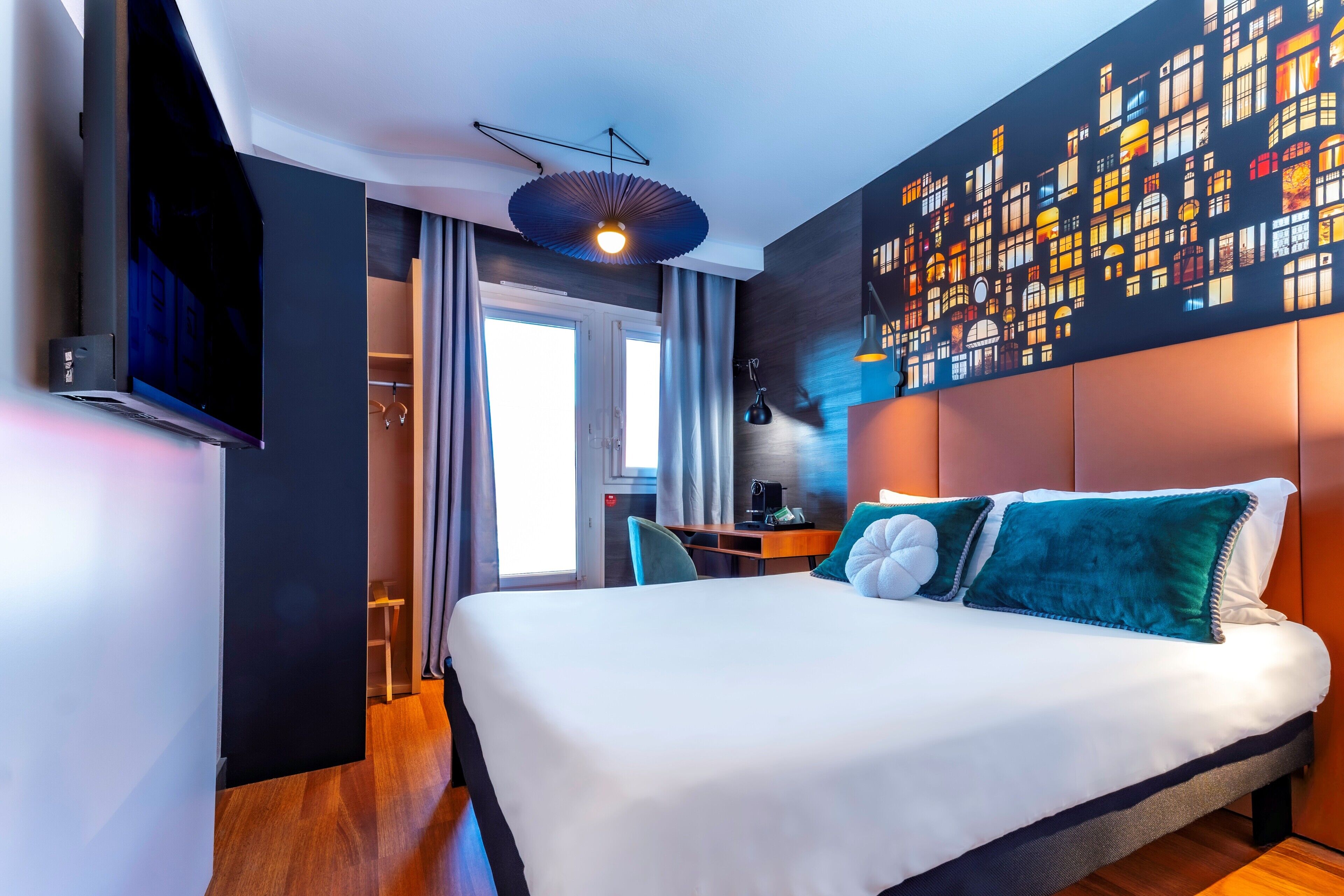 A modern hotel room with a large bed, a flat-screen TV, a desk with a chair, and a unique wall art piece.