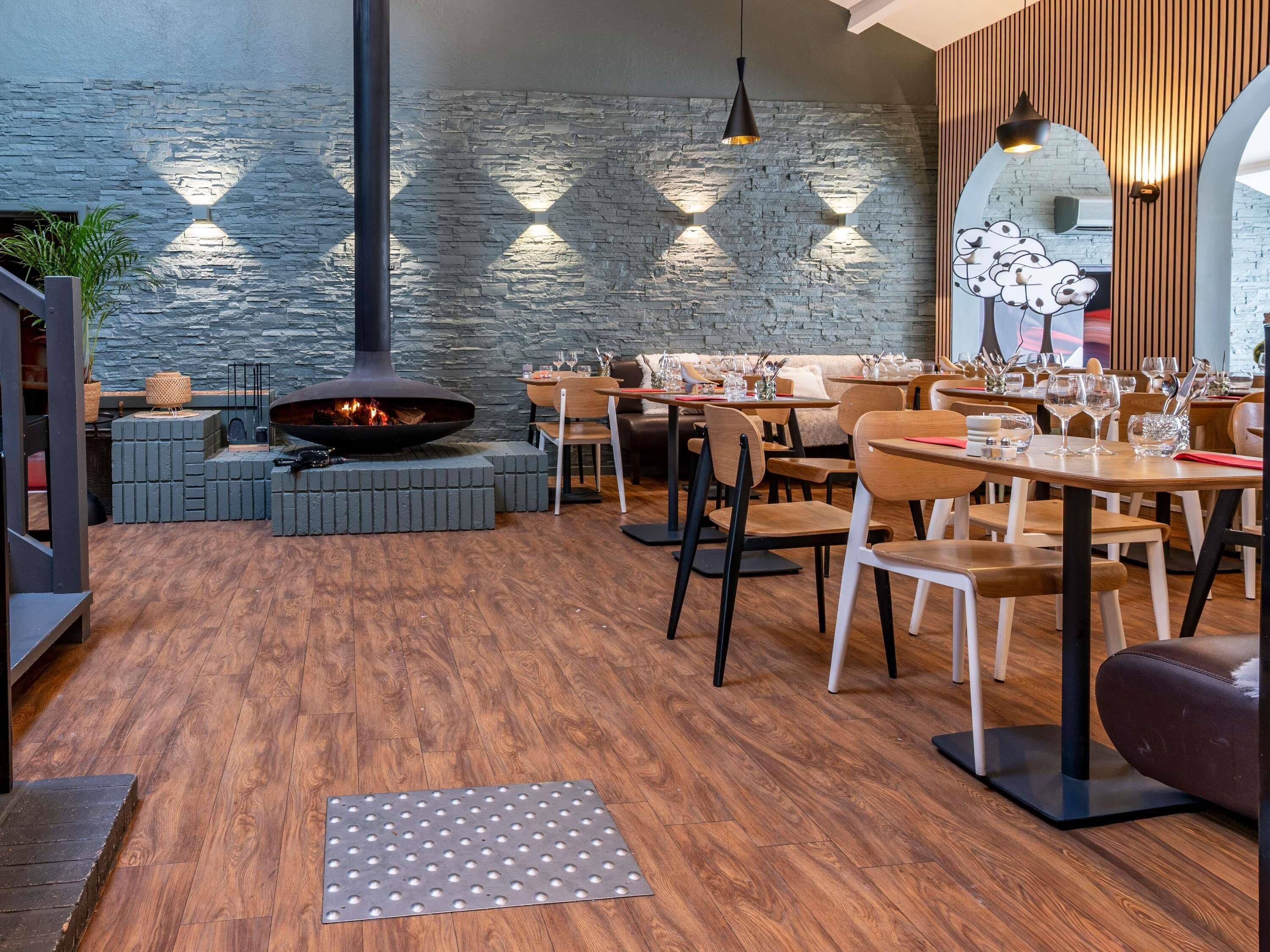 A modern dining area with a stone wall, a central fire feature, and wooden flooring.