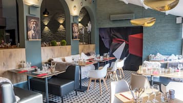 A modern restaurant interior with high tables, comfortable seating, and decorative wall art.
