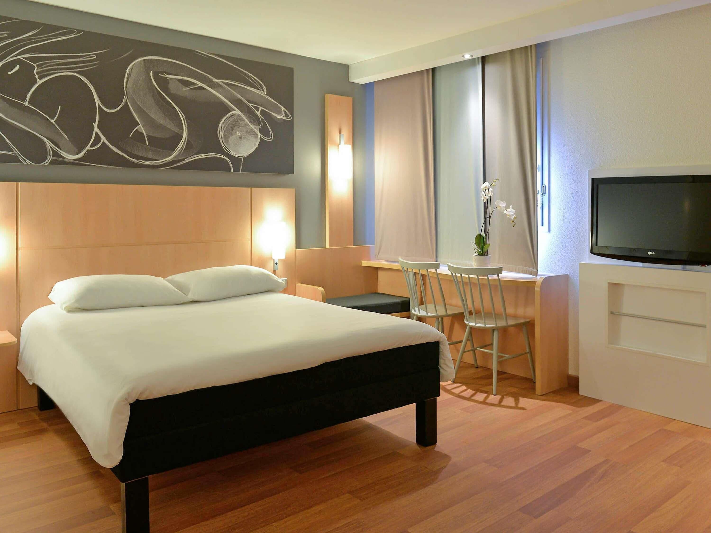 Habitació d'hotel amb llit, escriptori, cadira, televisió i una obra d'art penjada a la paret.