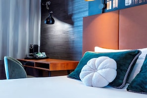 A hotel room with a bed, a desk, a chair, a lamp, and a nightstand.