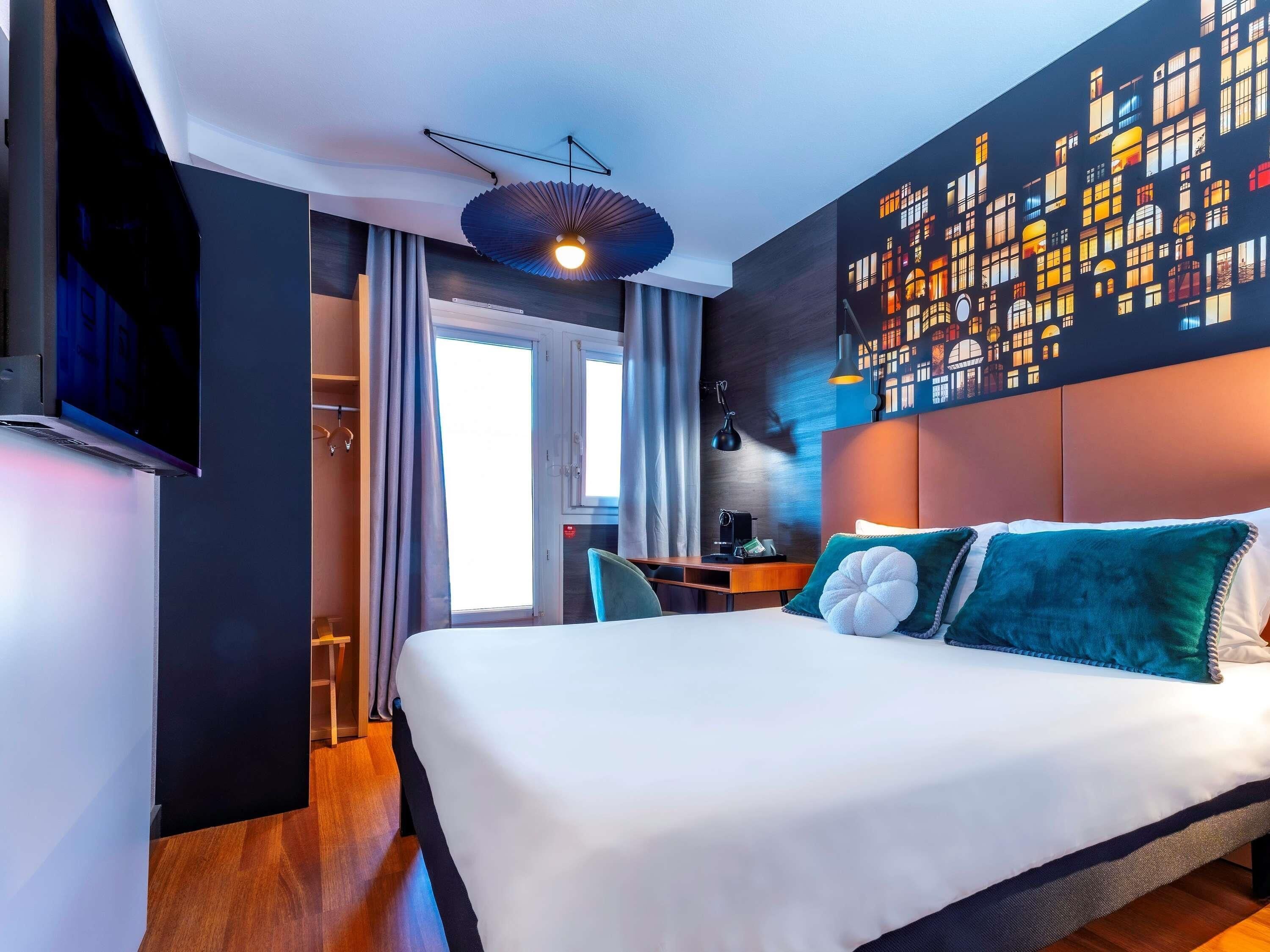 Habitación de hotel moderna con una cama grande, un escritorio y un mural con vista a la ciudad.