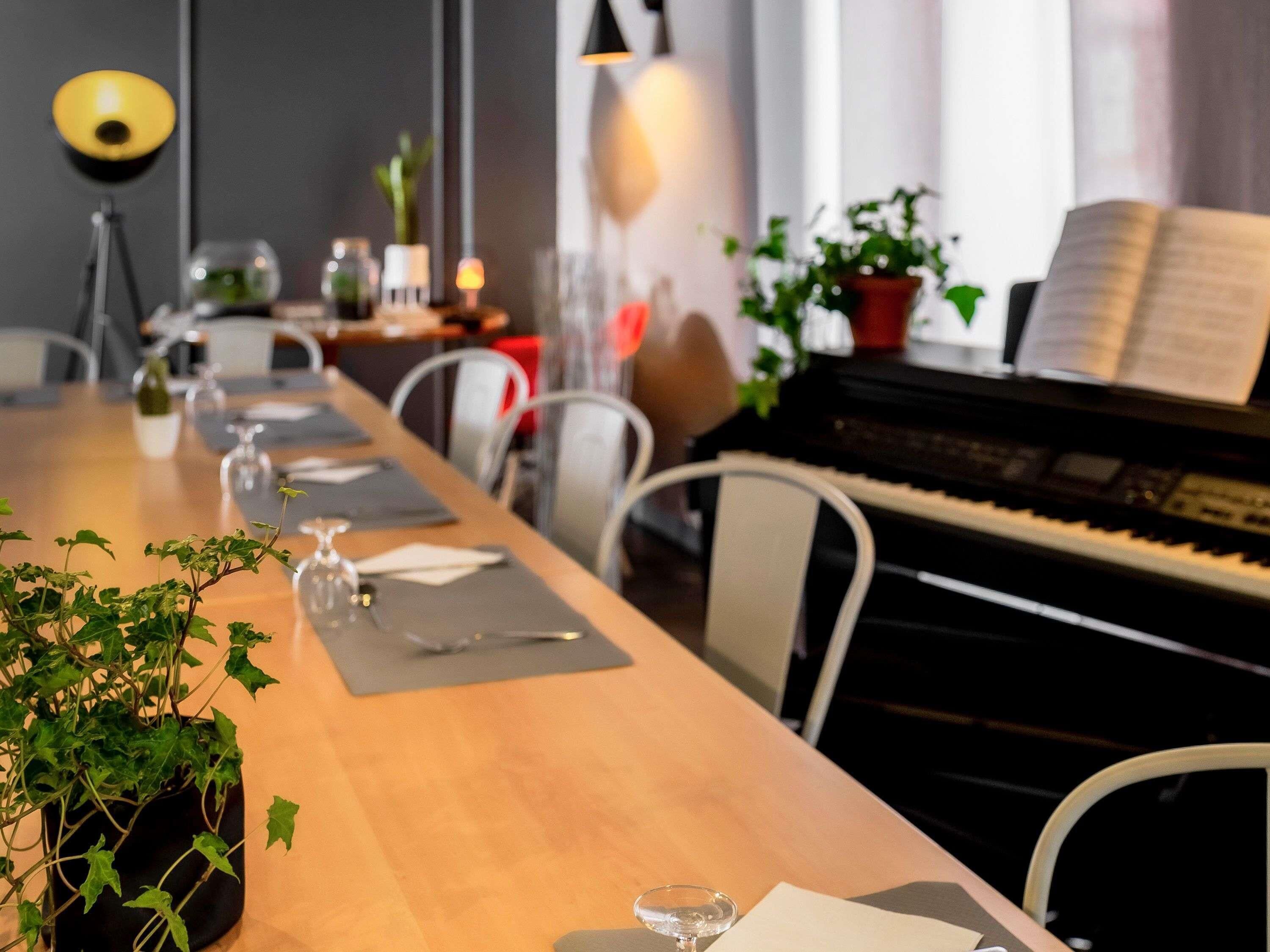 A dining area with a piano, chairs, a table set with plates, glasses, and a plant.