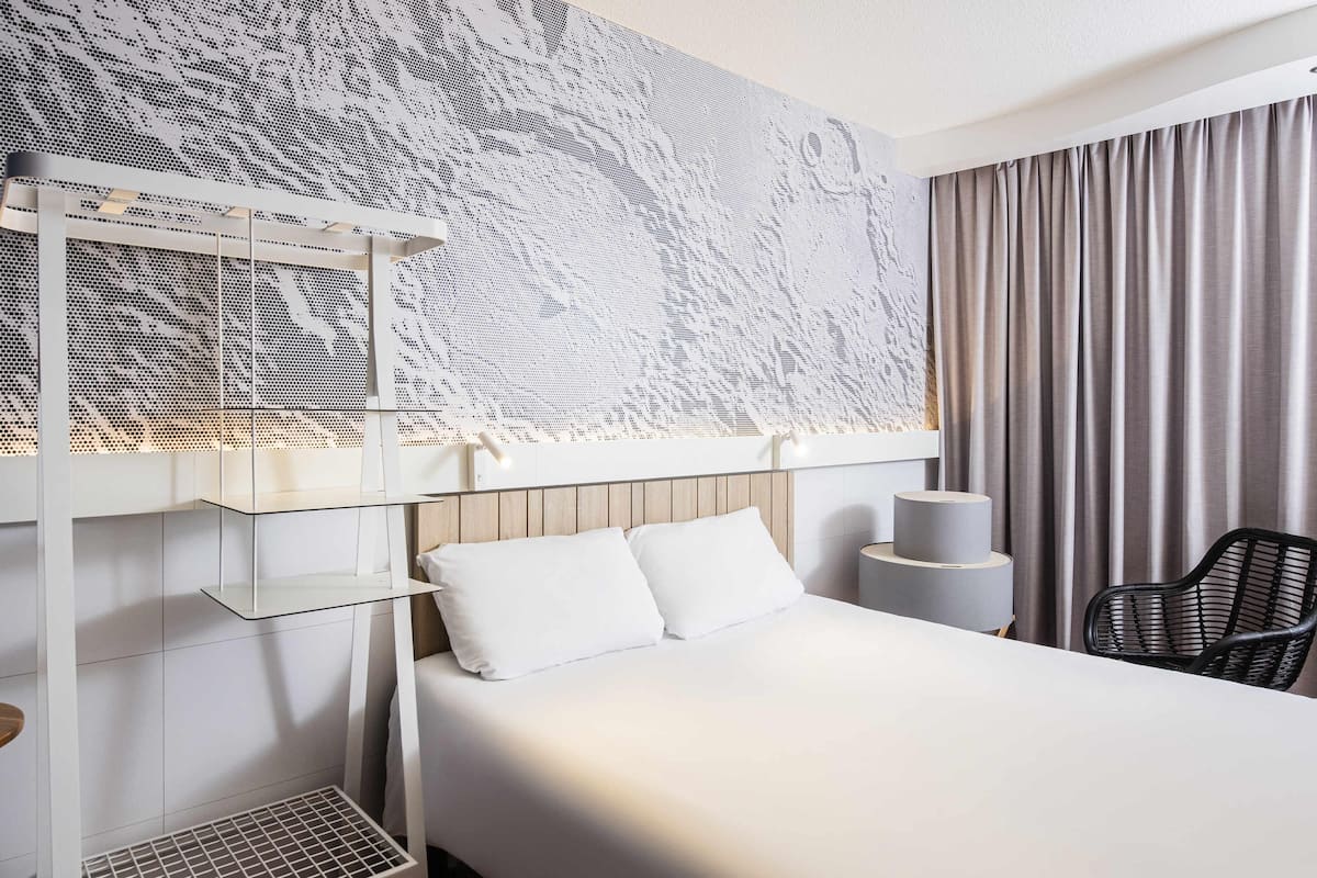Ett hotellrum med en våningssäng, ett skrivbord, en stol och ett stort fönster med gardiner.