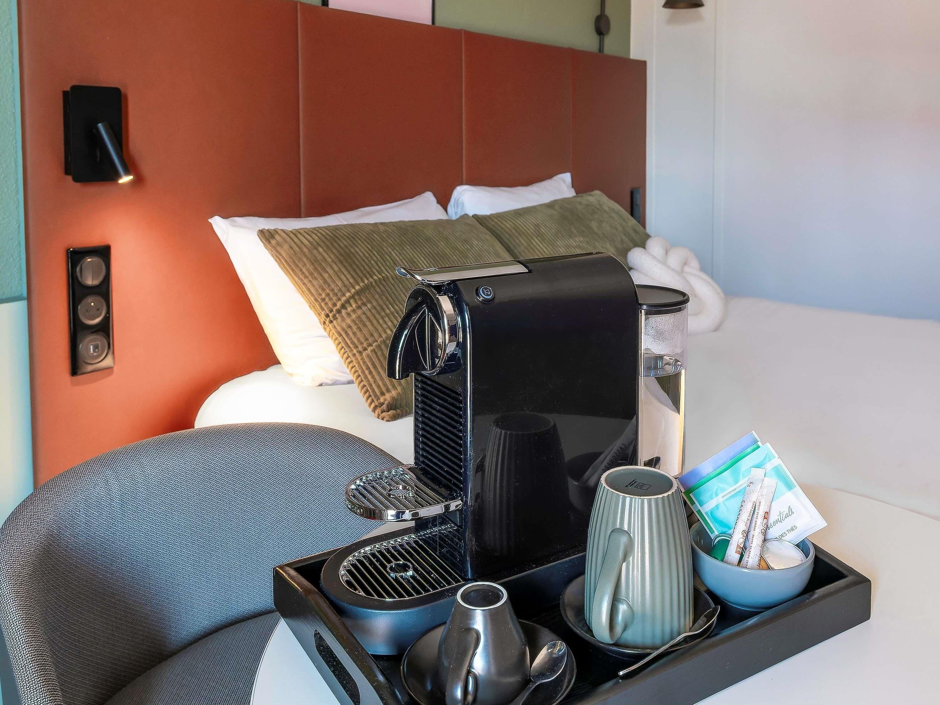A hotel room with a bed, a coffee machine, a tray with a mug, a bowl, and some cards.