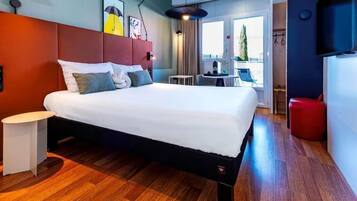 A modern hotel room with a large bed, a small table, a chair, and a TV.