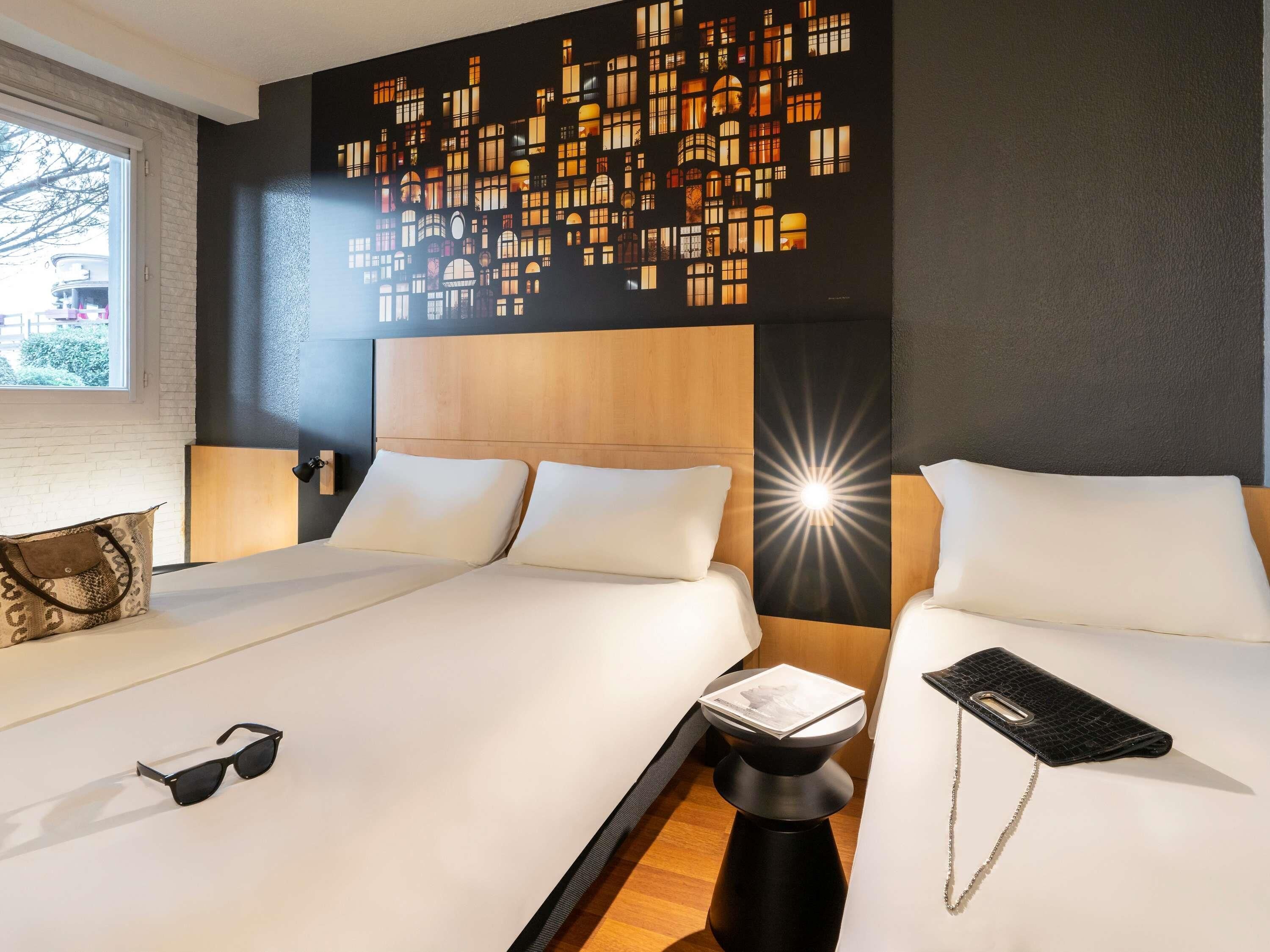 A hotel room with two beds, a nightstand, a lamp, and a wall art piece.