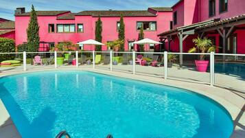 Ein Swimmingpool mit weißem Zaun, Liegestühlen und Kübelpflanzen.