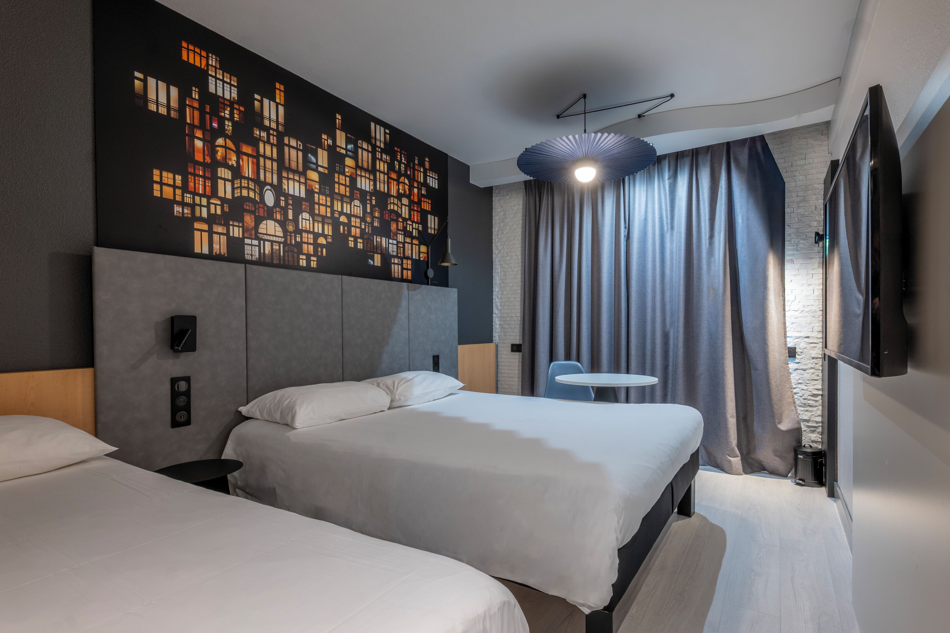 A modern hotel room with two beds, a large wall art piece, a flat-screen TV, and a small round table.