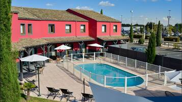 Ein rotes Gebäude mit Schwimmbad, Außenbereich und Parkplatz im Hintergrund.