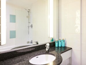 A bathroom with a sink, mirror, shower, and toiletries. - Novotel Bristol Centre (Bristol)