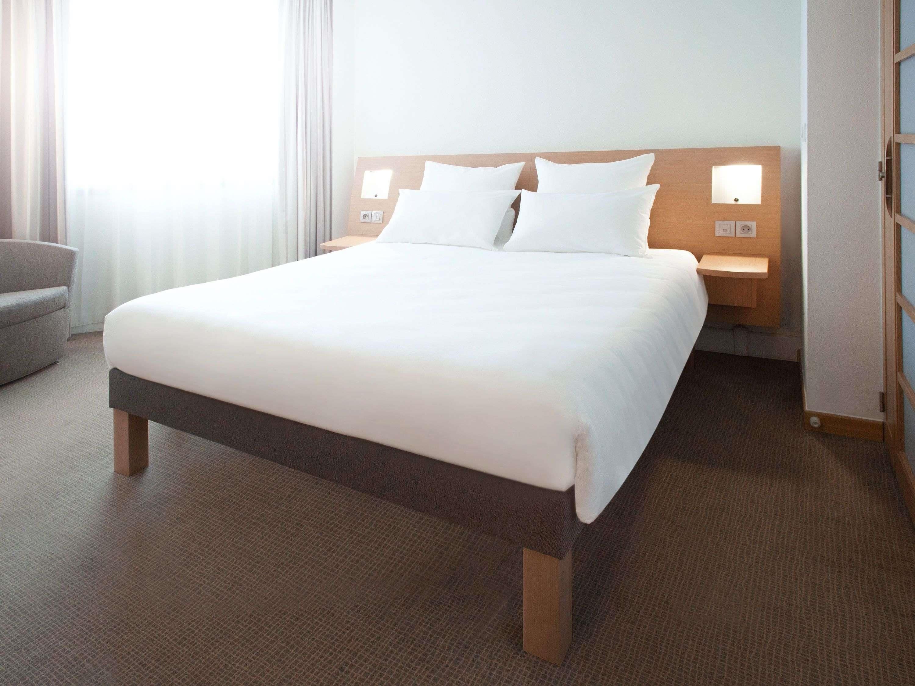 Une chambre d’hôtel avec un grand lit, une table de chevet, une chaise et une fenêtre avec des rideaux.