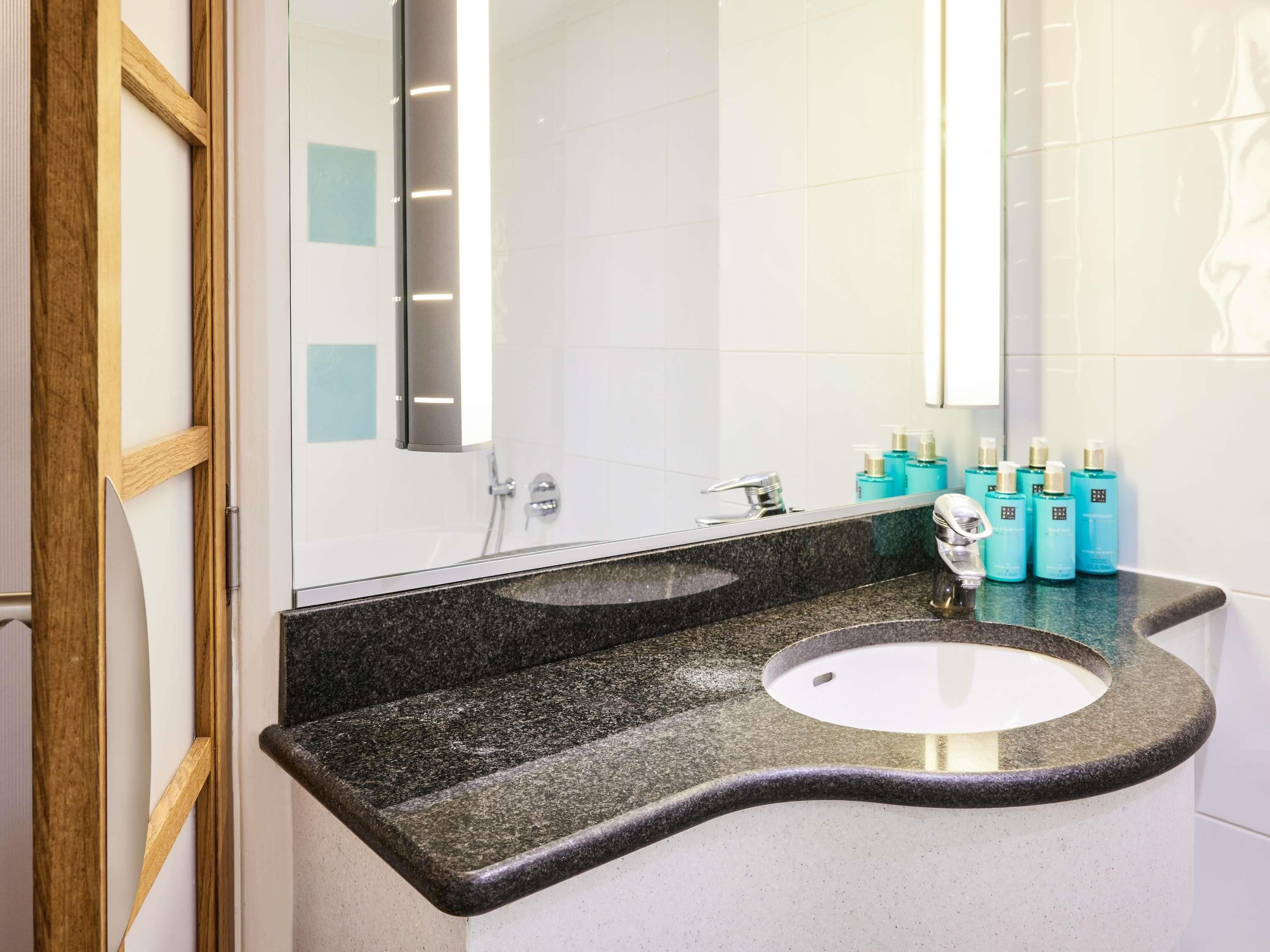 Un bagno con un piano di lavoro in granito, un lavandino e uno specchio. Sono presenti articoli da toilette sul piano.