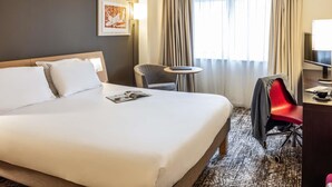 A hotel room with a large bed, a desk, a chair, and a window with curtains. - Novotel Bristol Centre (Bristol)