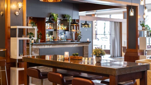 A bar area with a long counter, multiple hanging pendant lights, and a variety of bottles and glasses on shelves. - Novotel Bristol Centre (Bristol)