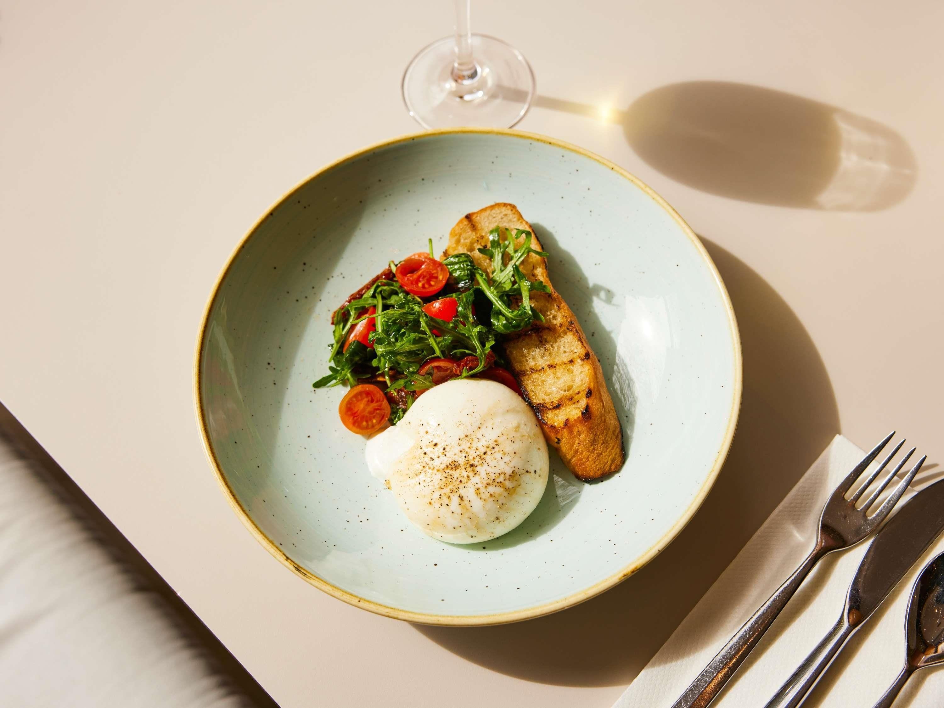 A plate with a poached egg, grilled bread, and a salad on a table.