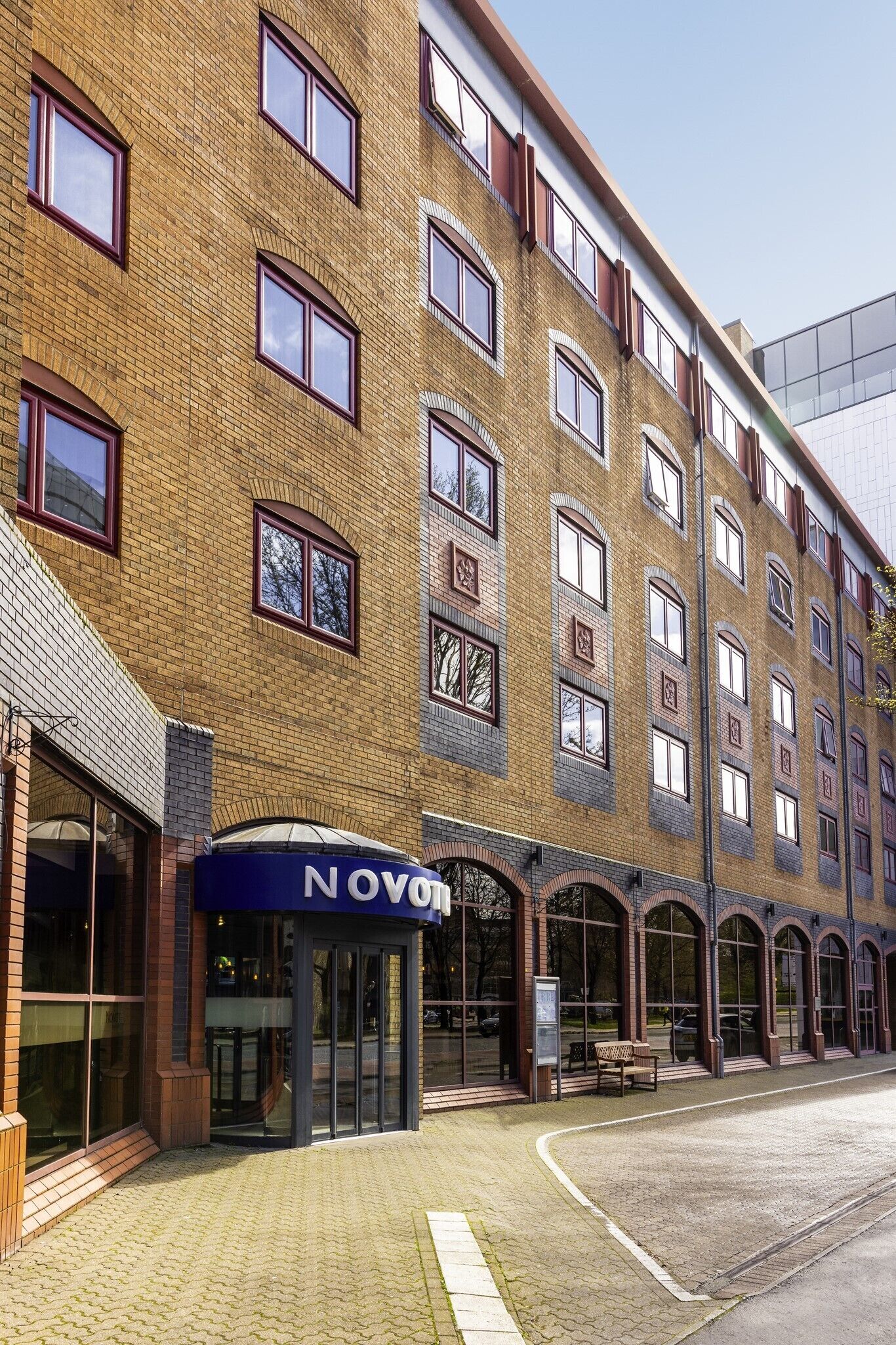 A multi-story building with a brick facade, large windows, and a blue awning with the name "NOVOM".