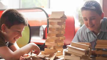 Two children playing with wooden blocks, with a red chair and a window in the background.