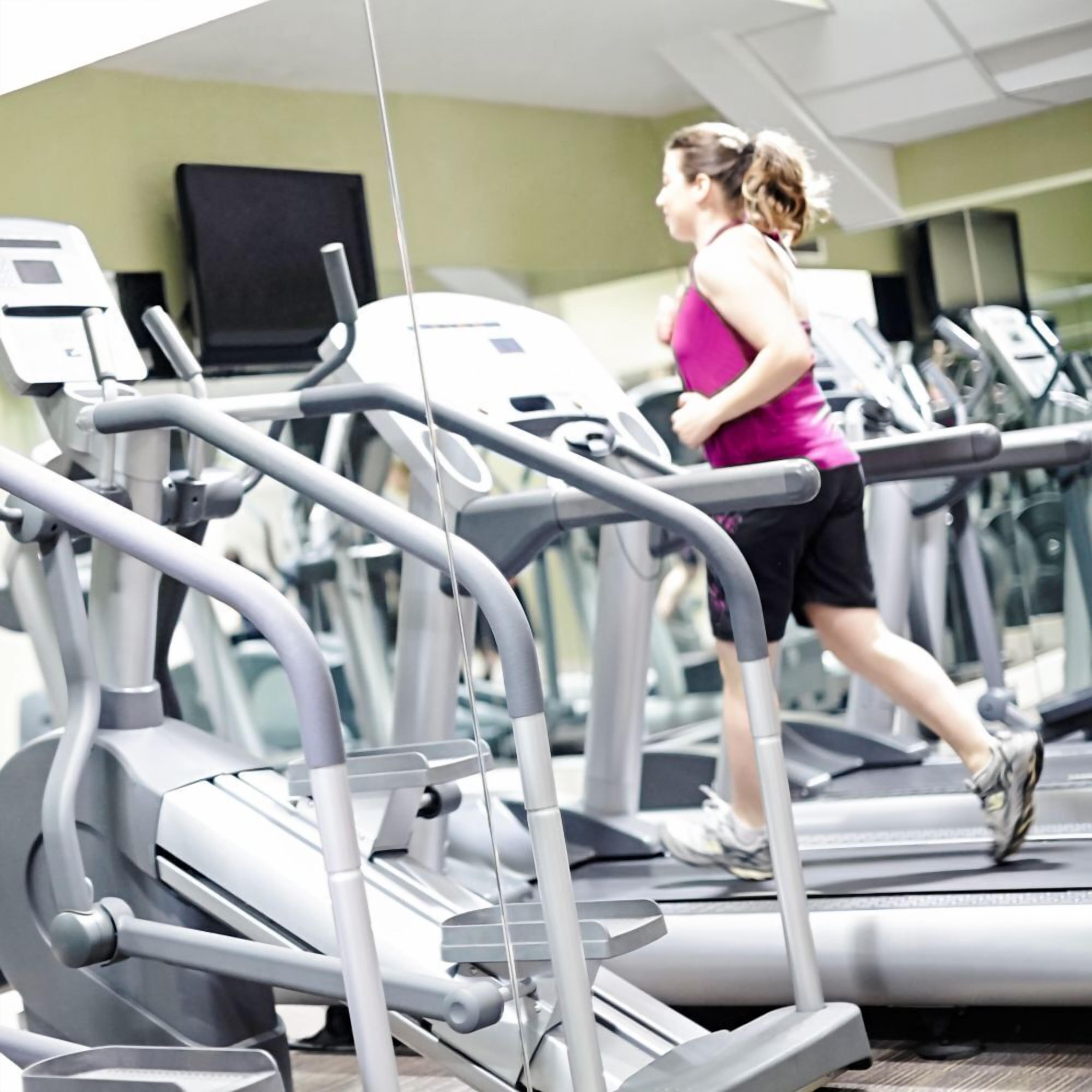 Un gimnasio con varias cintas de correr y una persona corriendo en una de ellas.