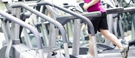 Un gimnasio con varias cintas de correr y una persona corriendo en una de ellas.