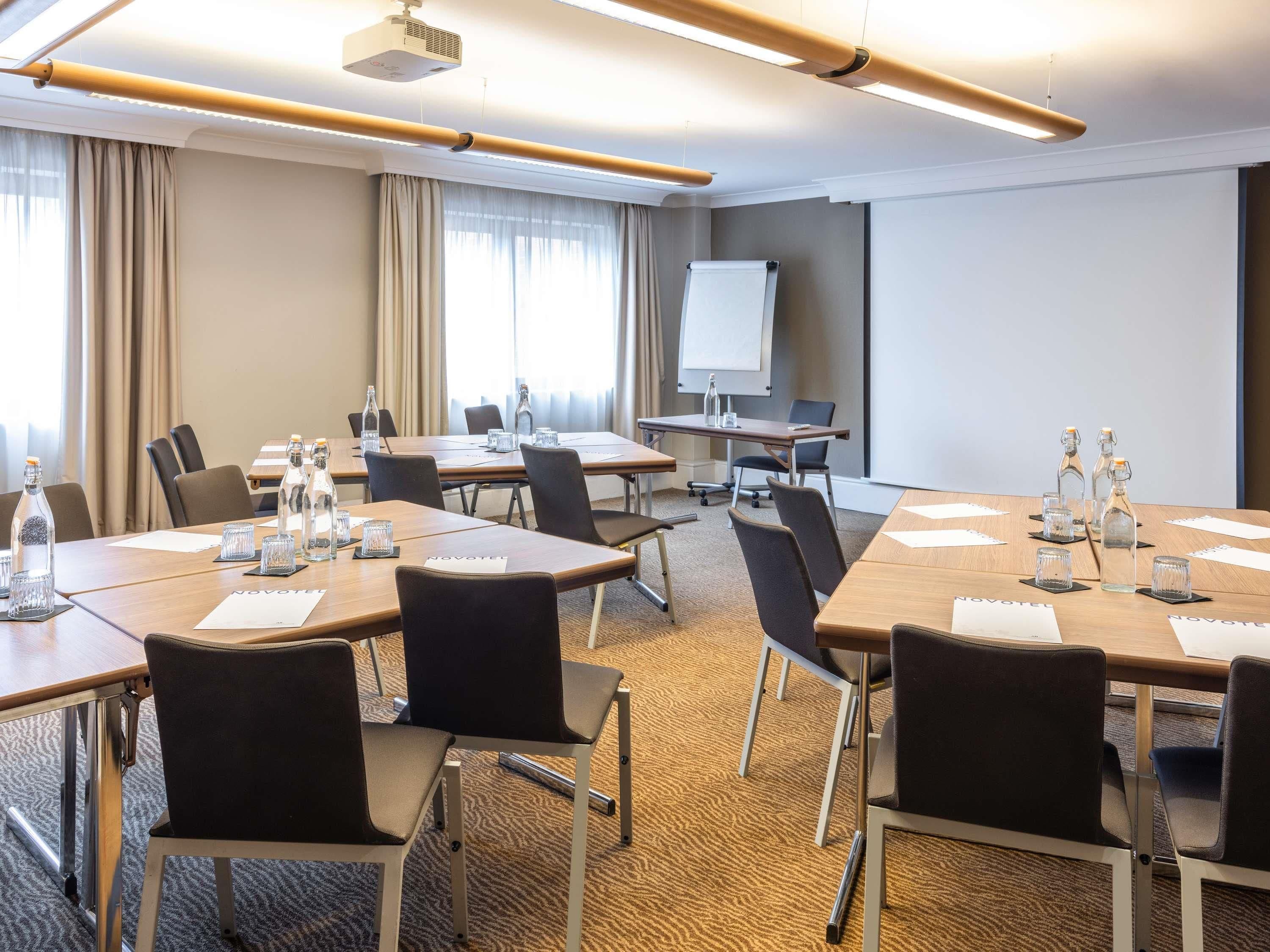 A conference room with multiple tables, chairs, a projector, and a whiteboard.