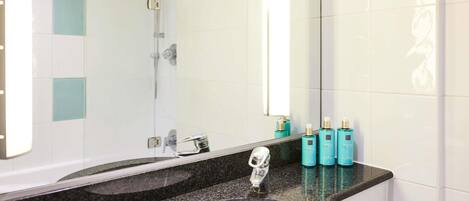 Un baño con lavamanos, espejo, ducha y artículos de aseo.